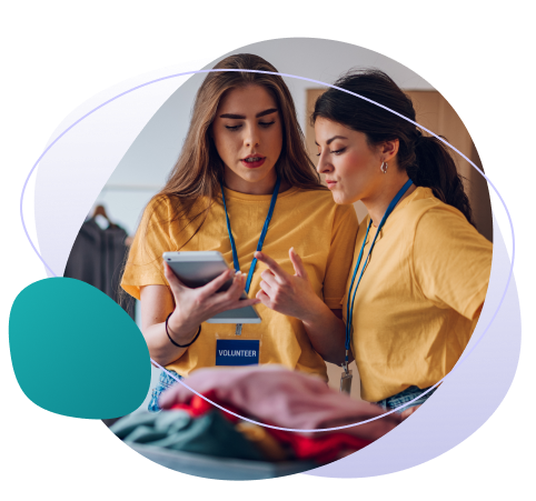 Two women volunteering and talking to each other while looking at something on a tablet.